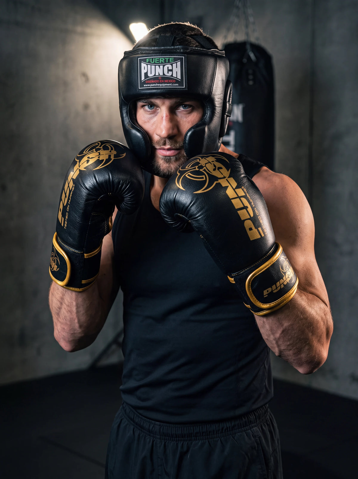 Male boxer wearing the Punch Equipment boxing sparring kit — Fuerte Mexican open-face head gear and black and gold Urban Haymaker 16oz gloves, in guard position in a gym