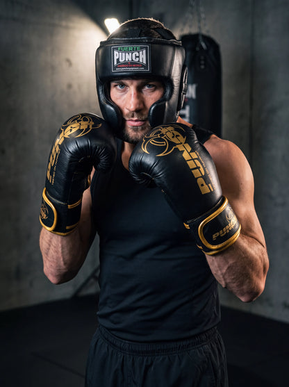 Male boxer wearing the Punch Equipment boxing sparring kit — Fuerte Mexican open-face head gear and black and gold Urban Haymaker 16oz gloves, in guard position in a gym